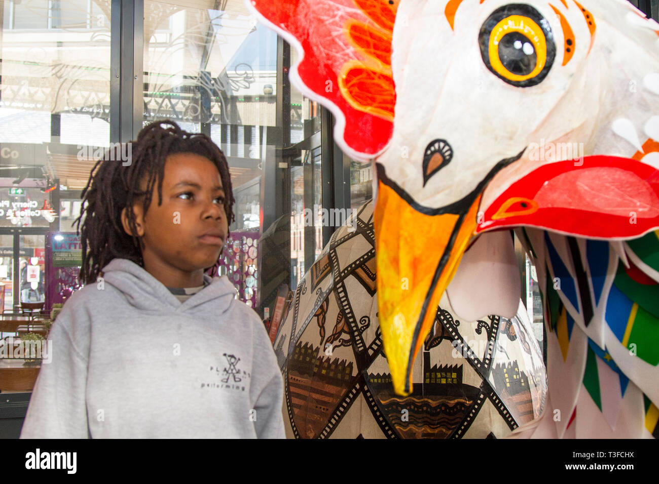 Riesige Ostern Pappmaché übergroßen Huhn auf dem Display in der Innenstadt. TADIWA CHAPARADZA (MR) 10 Jahre alt ist fasziniert von der großen Hahnenskulptur Papier-Mache. Ostern festliche Tierfiguren auf dem Display Stehen bei zwei Meter hoch, die Attraktionen sind außerhalb Preston Market platziert. Keith Ogden, ein lokaler Künstler, ist der Mann hinter der handbemalten Attraktion. Die Eier sind Themen rund um das industrielle Erbe der Stadt und Lancashire Landschaften. Preston Markets werden die Riesen-Ostereier für Selfie-Wettbewerb über die Osterferien ausstellen. Stockfoto