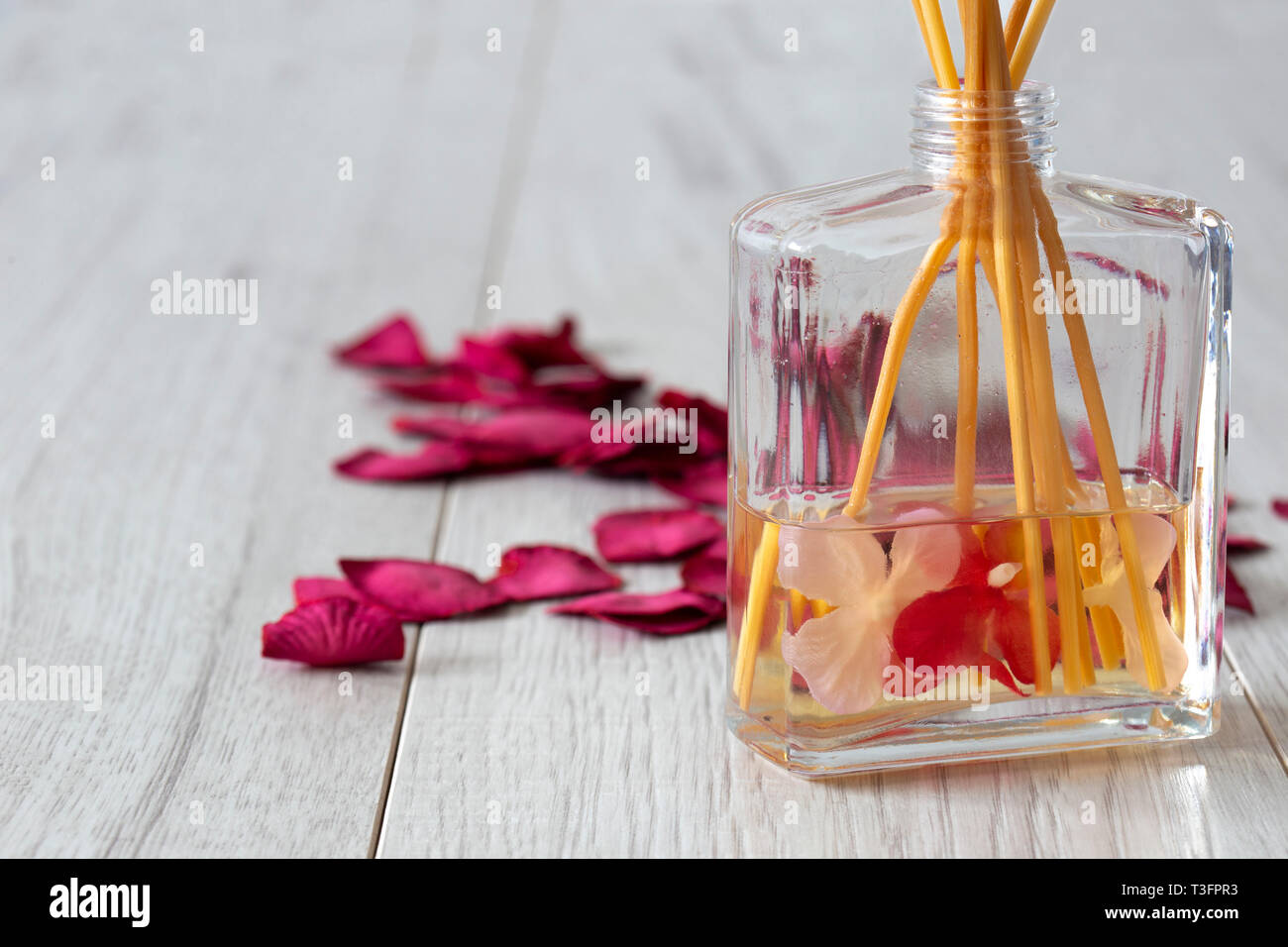 Reed Diffuser mit Duft im Glas mit Rosenblättern auf einem grauen