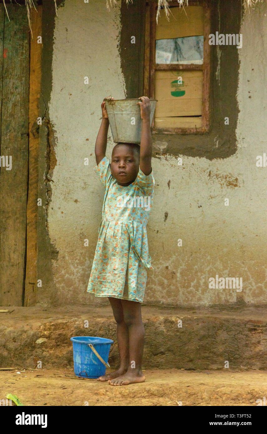 Barfuß malawische Mädchen, dass Eimer mit Mais Mehl auf dem Kopf außerhalb ihrer Schlamm Haus in Chiphazi Dorf Stockfoto