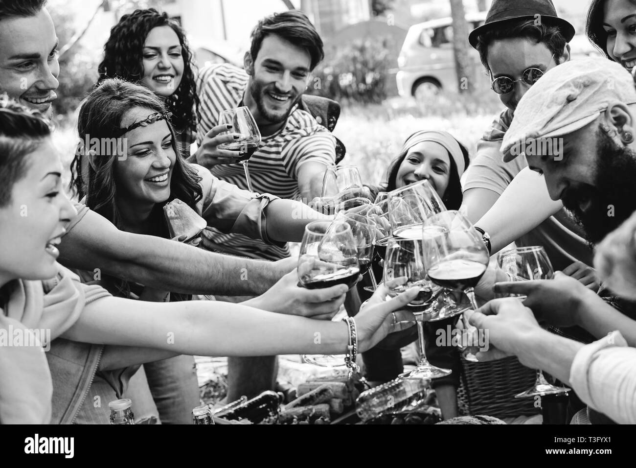 Gruppe von Menschen jubeln mit roten Gläsern Wein - Glückliche junge Freunde genießen, Picknick im Park mit Essen e trinken - Schwarz und Weiß bearbeiten Stockfoto