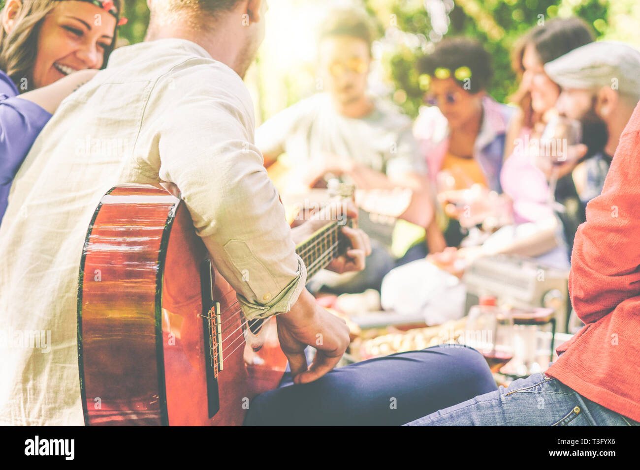 Eine Gruppe von Freunden ein Picknick im Park im Freien - Glückliche junge Gehilfen mit Pic-nic Gitarre spielen, Singen, Wein trinken und Essen Stockfoto