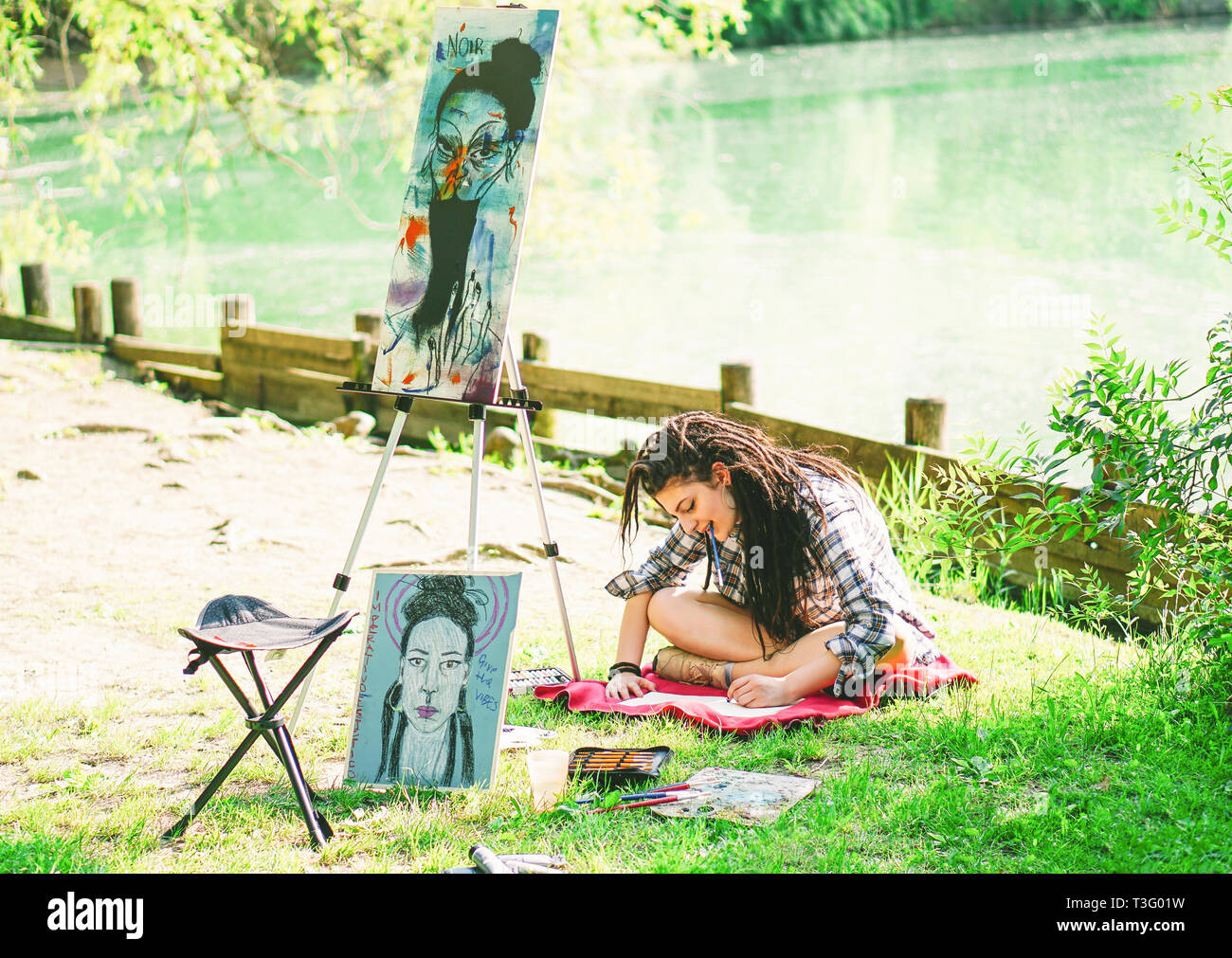 Junge Künstlerin Mädchen Zeichnung Entwurf der nächsten Malerei an der Park in der Nähe von Lake - Maler Frau mit Dreadlocks Frisur arbeiten auf ihre Kunst in der Stadt im Freien Stockfoto