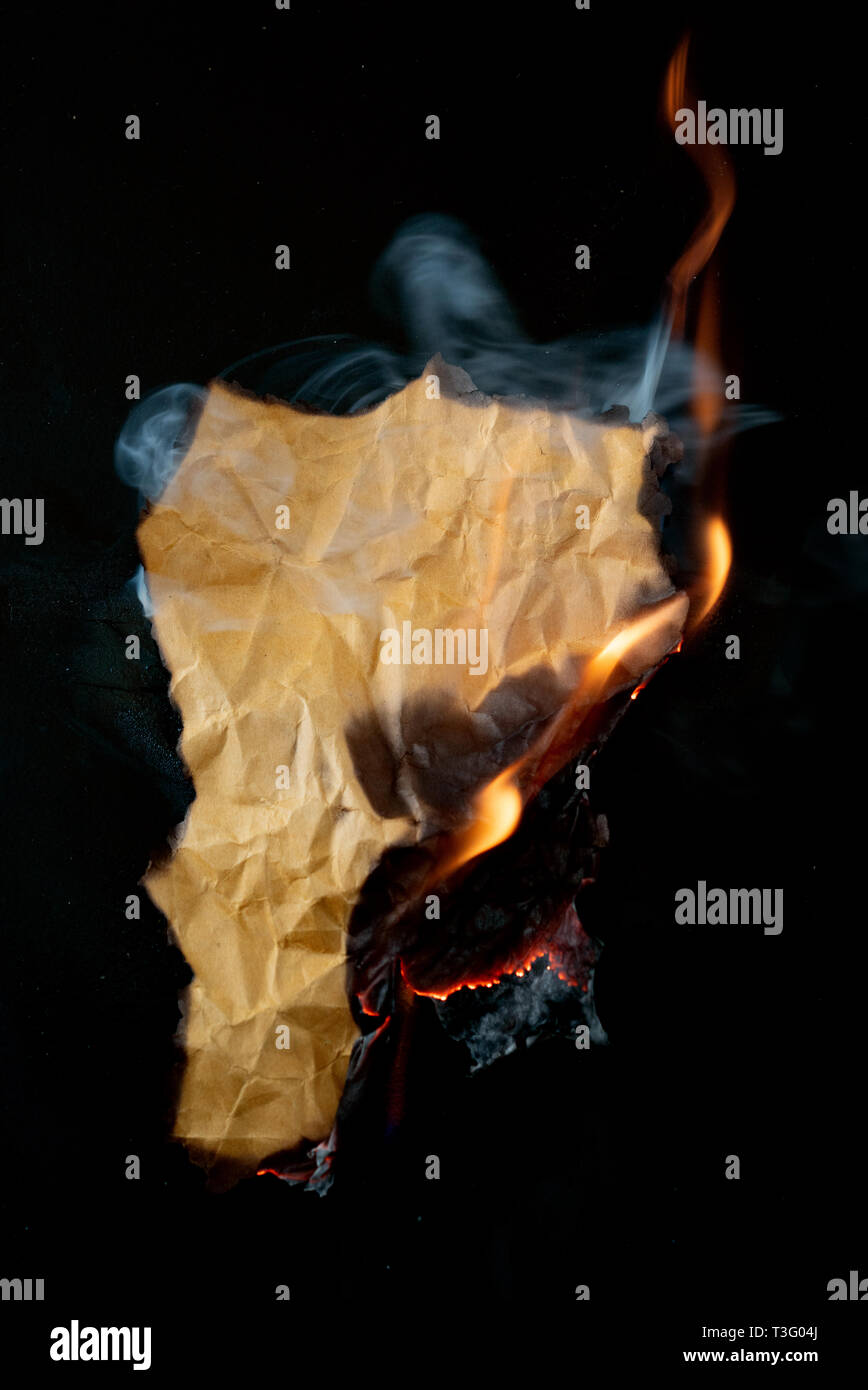 Brennende Stück zerknittertes Papier auf schwarzem Hintergrund Stockfoto