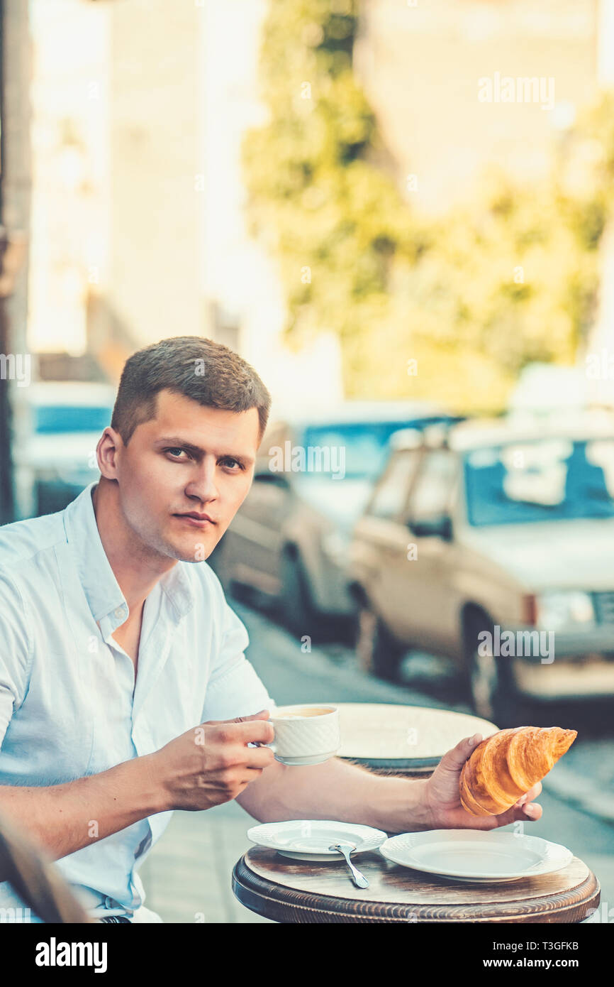 Mann essen und trinken Kaffee in Street Cafe. Macho genießen Tasse Kaffee und Croissant auf Urban outdoor. Essen und Trinken Konzept Stockfoto