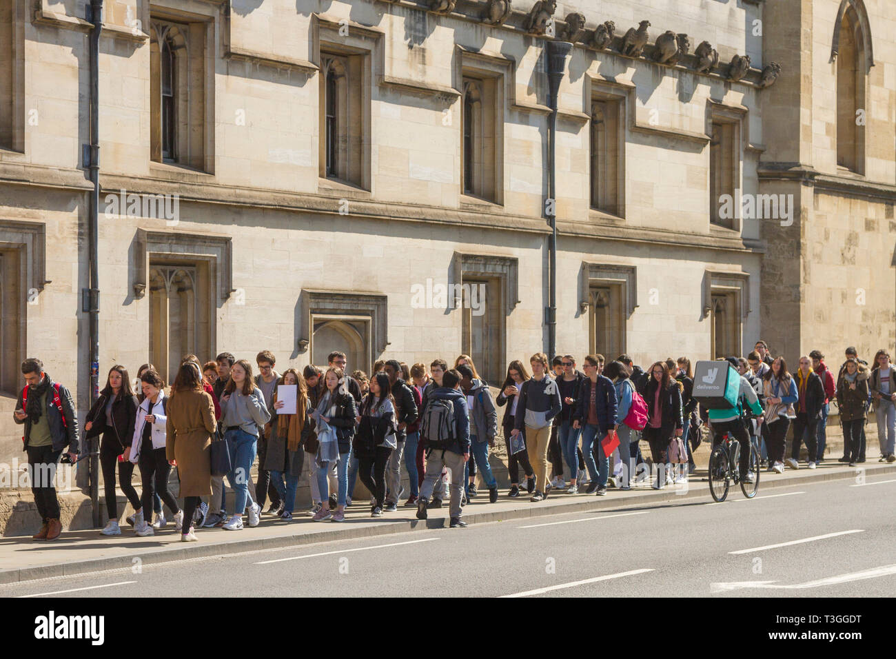 Eine Gruppe von Schülerinnen und Schülern gehen Sie die High Street, Oxford Vergangenheit Magdalen College als Deliveroo rider Zyklen Vergangenheit Stockfoto