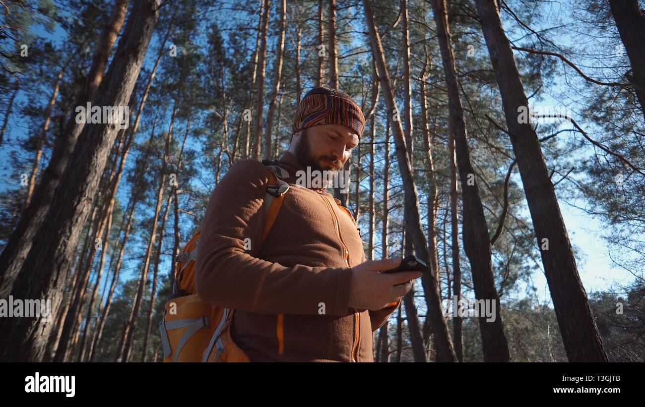 Thema Tourismus und Technologie. Jungen kaukasischen Mann mit Bart und Rucksack. Wandern touristische in einem Pinienwald verwendet die Technologie, Hand Handy Stockfoto