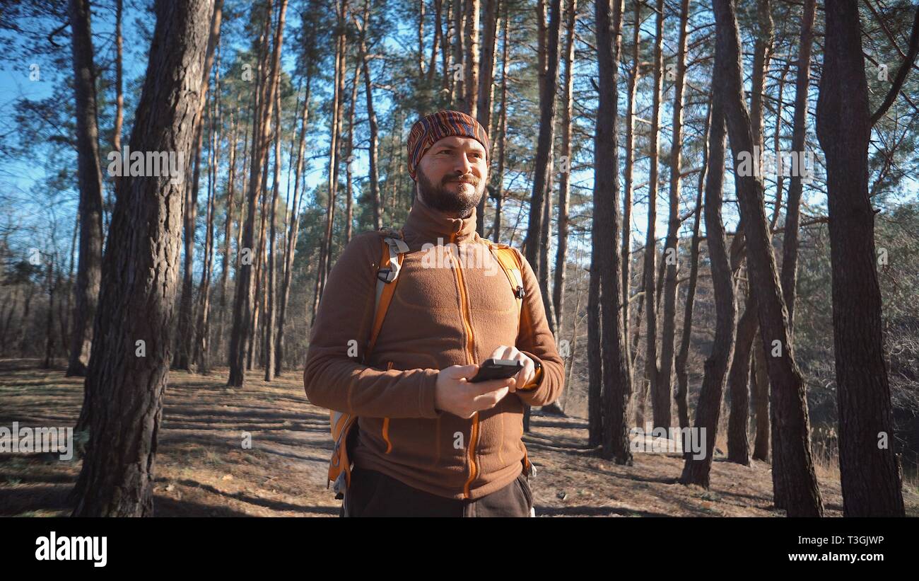 Thema Tourismus und Technologie. Jungen kaukasischen Mann mit Bart und Rucksack. Wandern touristische in einem Pinienwald verwendet die Technologie, Hand Handy Stockfoto