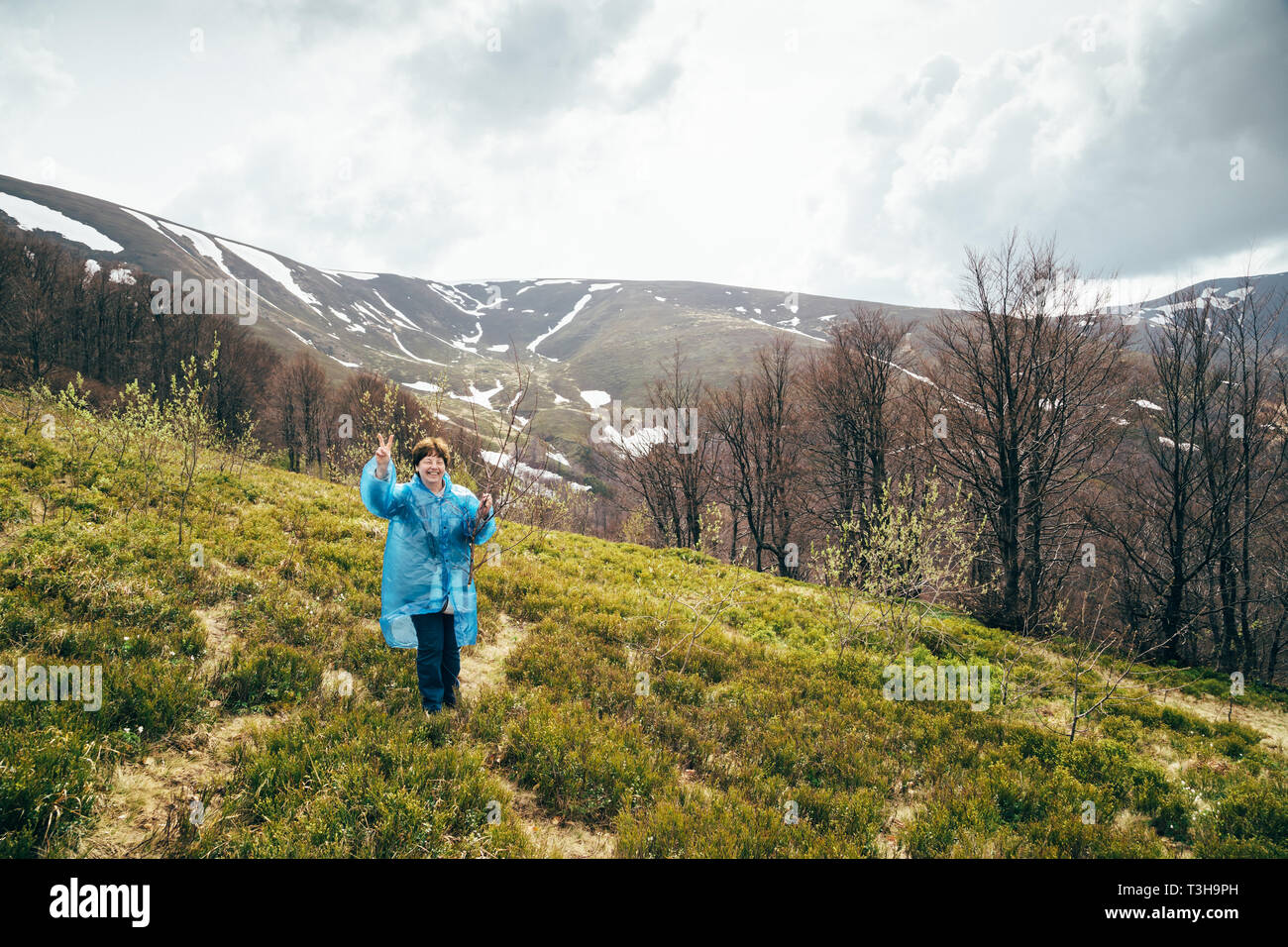 Glücklich lächelnde Traveller senior schöne Frau in Blau regen Jacke und Jeans in Berge umgeben von Wald, genießen die Stille und Harmonie der Natur Stockfoto