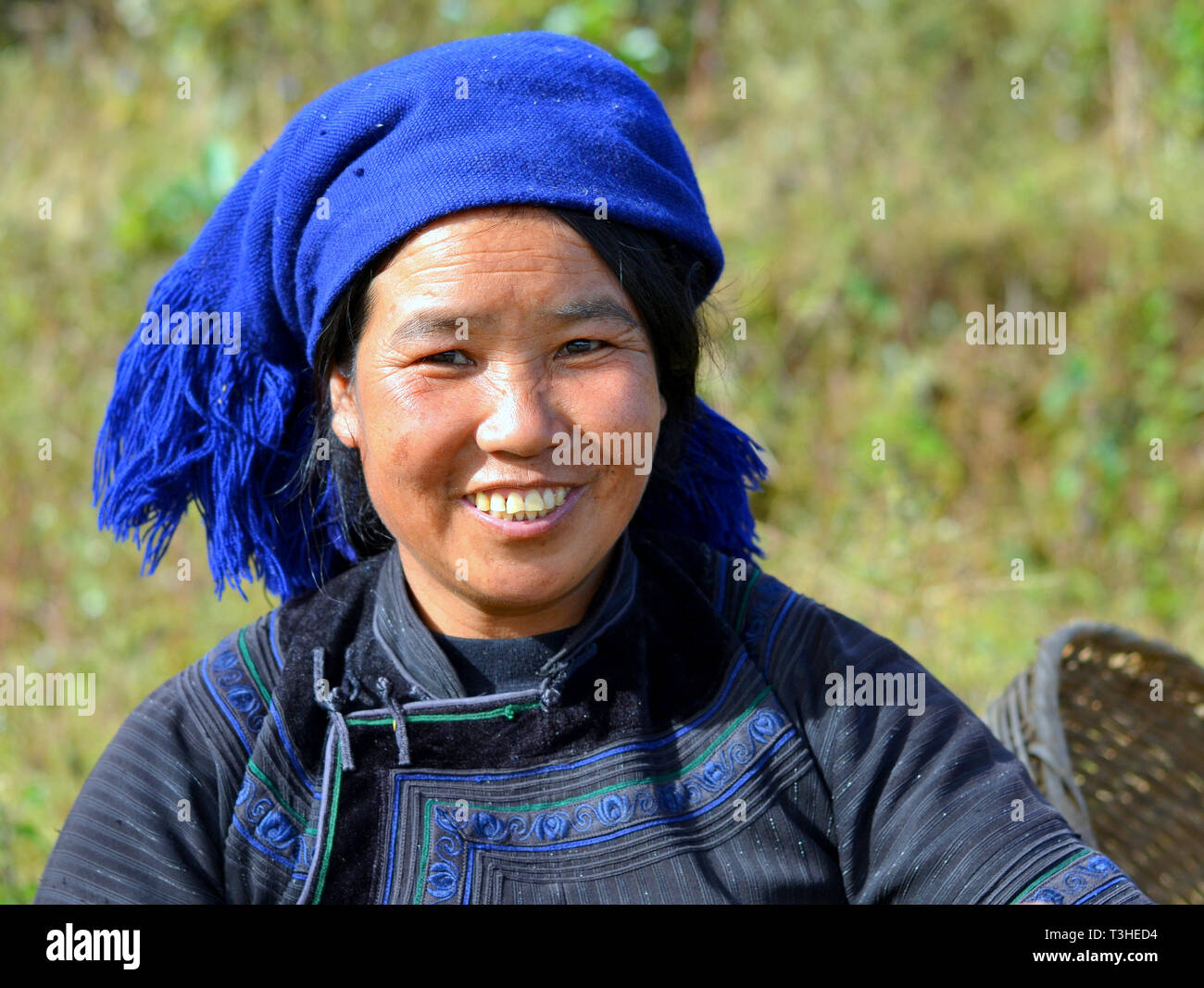 Junge Hani Frau (chinesische ethnische Minderheit) trägt eine schwarz-blaue traditionellen ethnischen Kleid mit blauem Kopftuch und Lächeln für die Kamera. Stockfoto