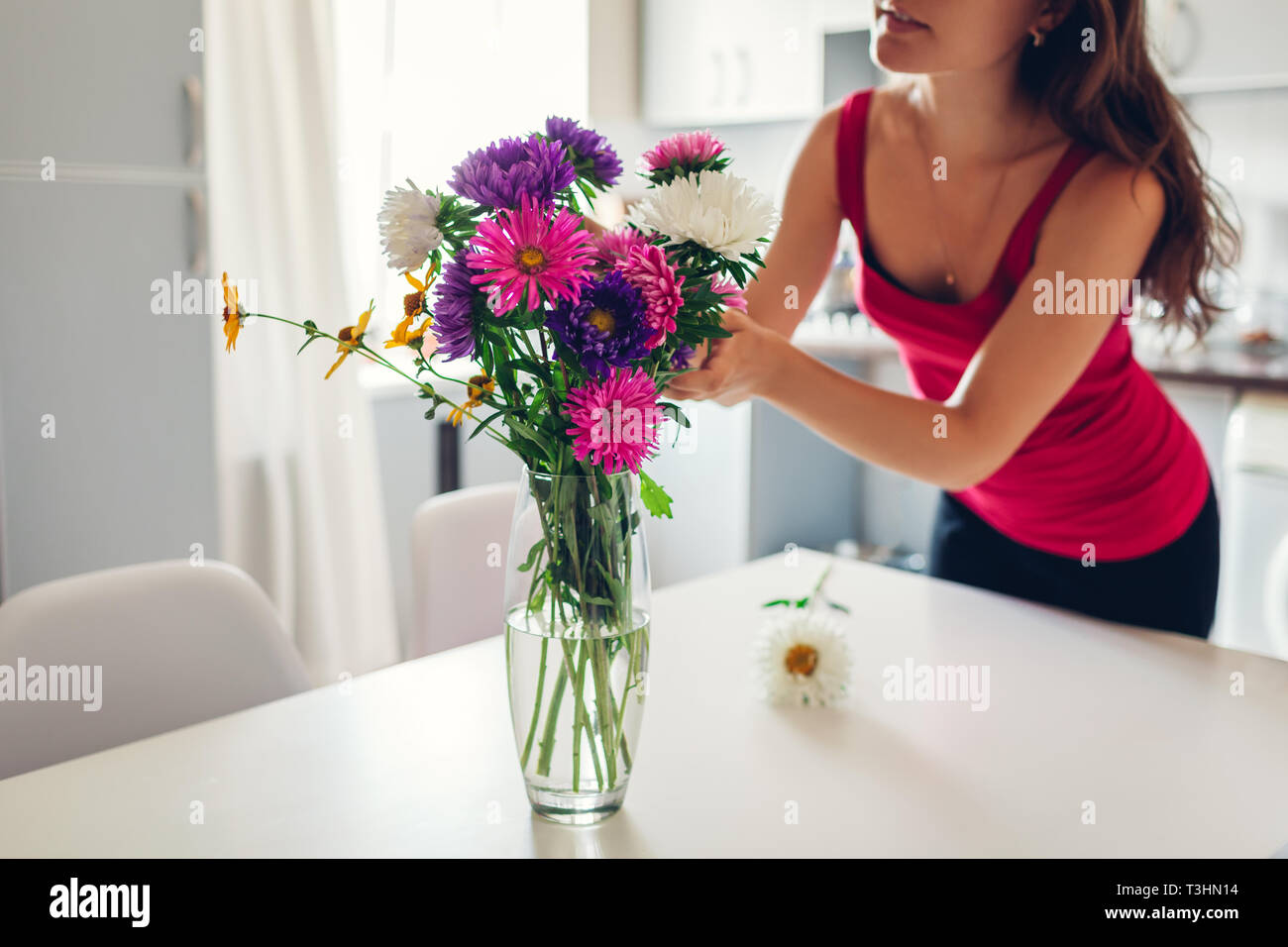 Frau setzt rosa Blumen in der Vase. Junge Hausfrau kümmert sich um die Gemütlichkeit in der Küche. Moderne Küche Design. Weiß und Silber Küche Stockfoto