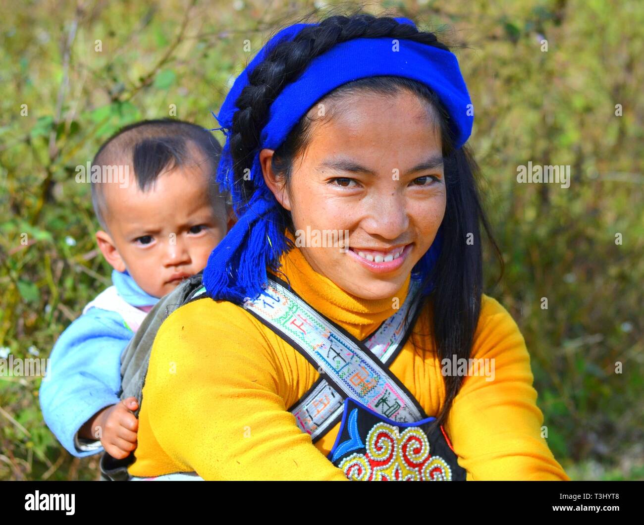 Junge Hani Frau (chinesische ethnische Minderheit) trägt ihr Baby auf dem Rücken in ein Baby sling mit ethnischen Design. Stockfoto