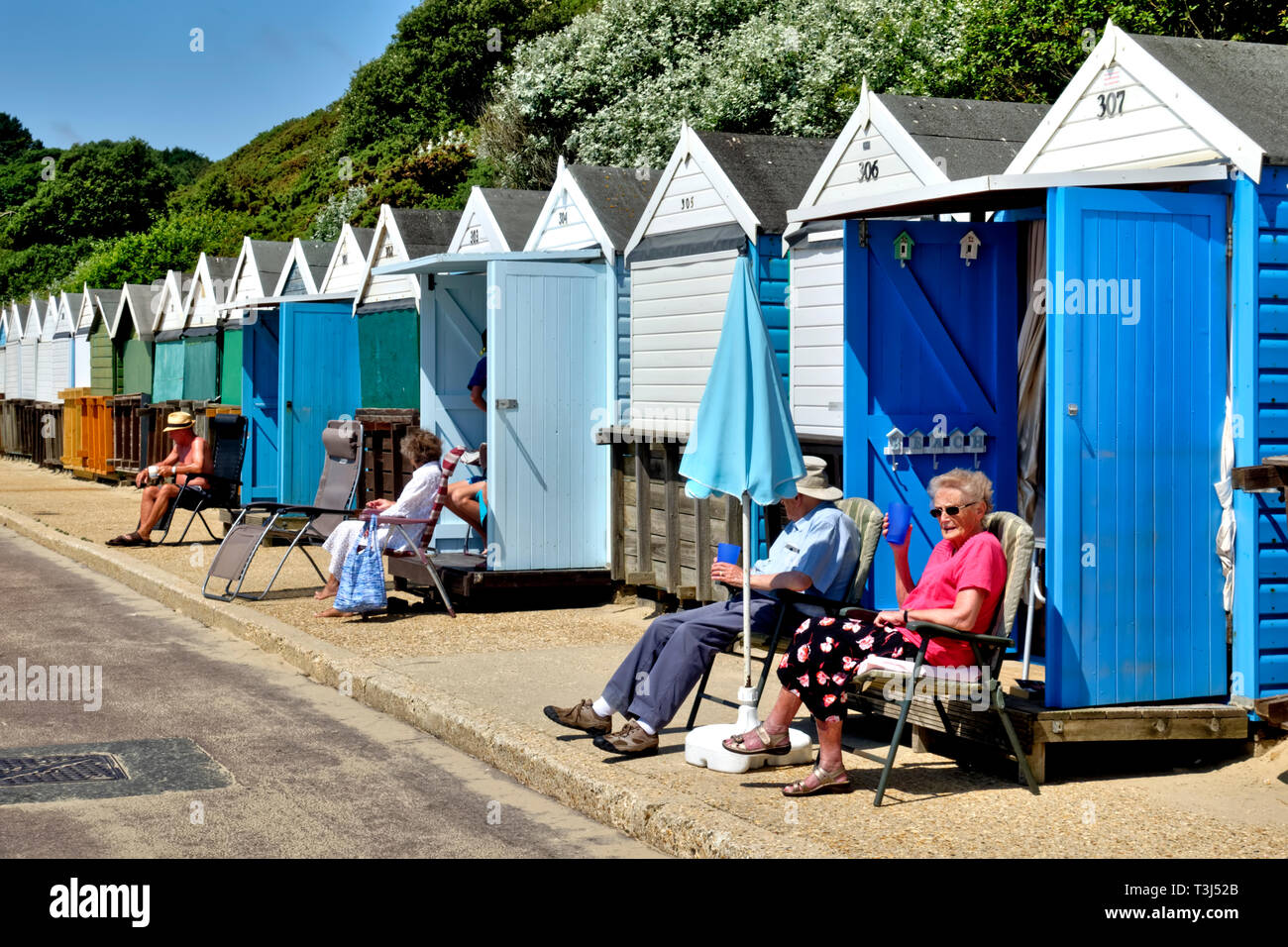 Menschen entspannen und die Sonne am Strand Hütten entlang West Spencer Court Promenade am Meer in Bournemouth, Dorset, England, Großbritannien genießen Stockfoto