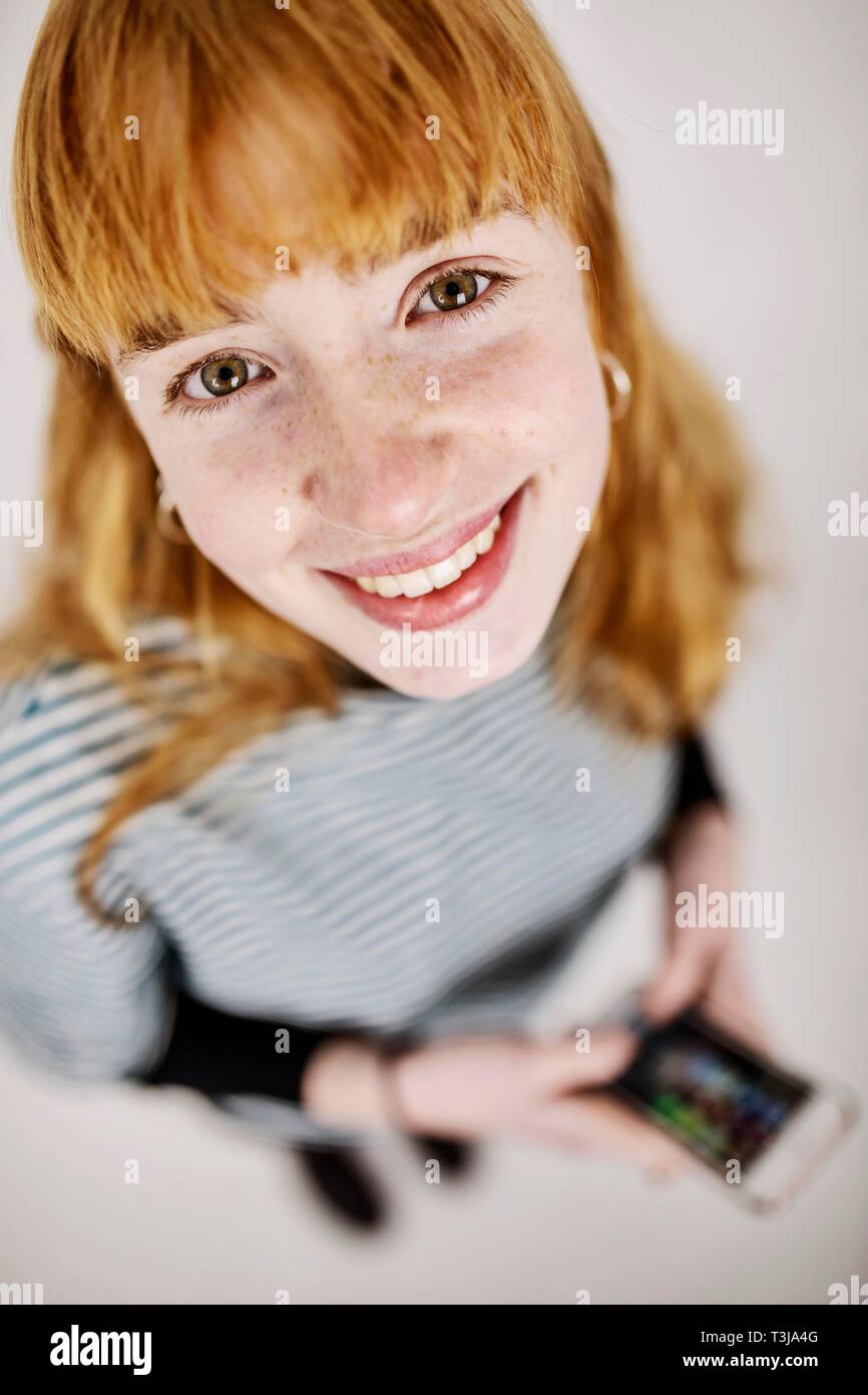 Mädchen, Teenager, Rothaarige, mit Smartphone in der Hand, lacht in die Kamera, studio Shot, Deutschland Stockfoto