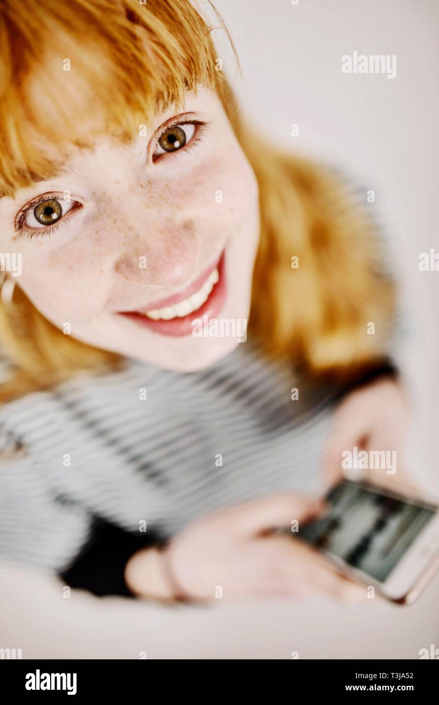 Mädchen, Teenager, Rothaarige, mit Smartphone in der Hand, lacht in die Kamera, studio Shot, Deutschland Stockfoto