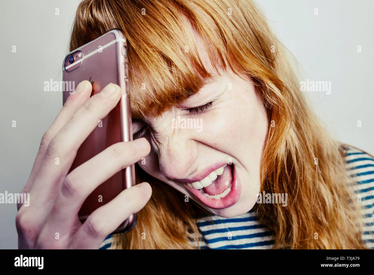 Mädchen, Teenager, Rothaarige, ihr Kopf in Verzweiflung schreien Smartphone, studio Shot, Deutschland Stockfoto