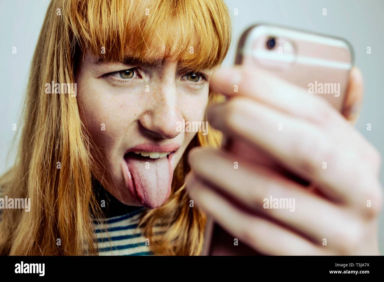 Mädchen, Teenager streckt die Zunge des Smartphones, studio Shot, Deutschland Stockfoto