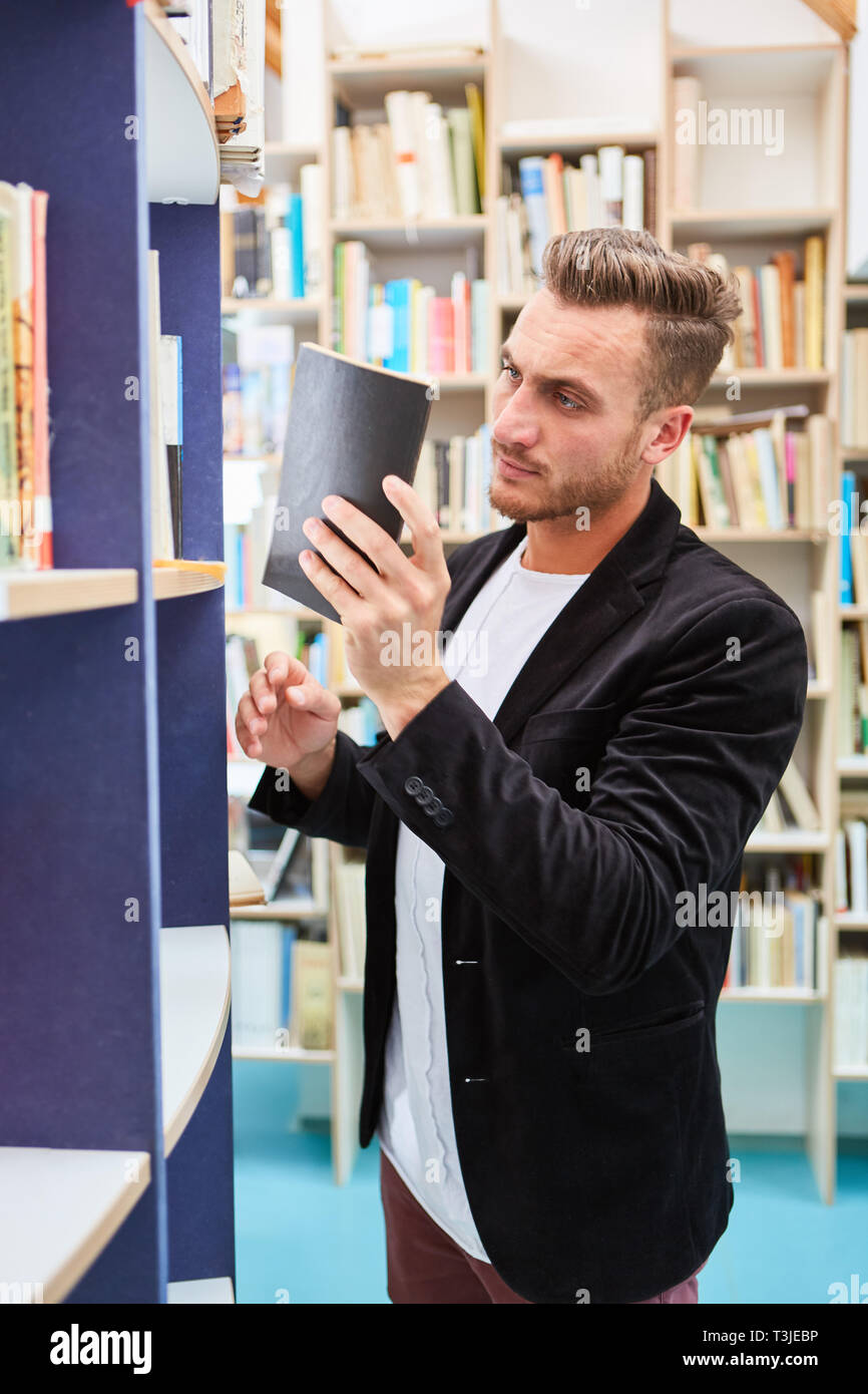 Dozent oder Bibliothekar mit einem Buch vor einem Bücherregal in der Universitätsbibliothek Stockfoto
