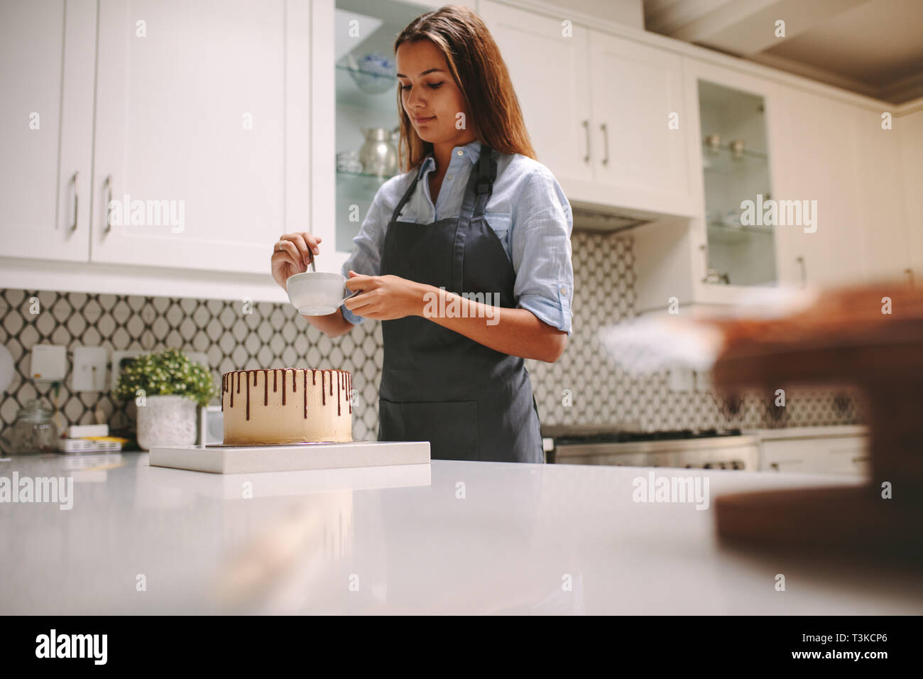 Frau Mischen flüssiger Schokolade in einer Schüssel, den Kuchen zu verzieren. Frau im Vorfeld vorbereiten Schokolade Kuchen zu Hause. Stockfoto