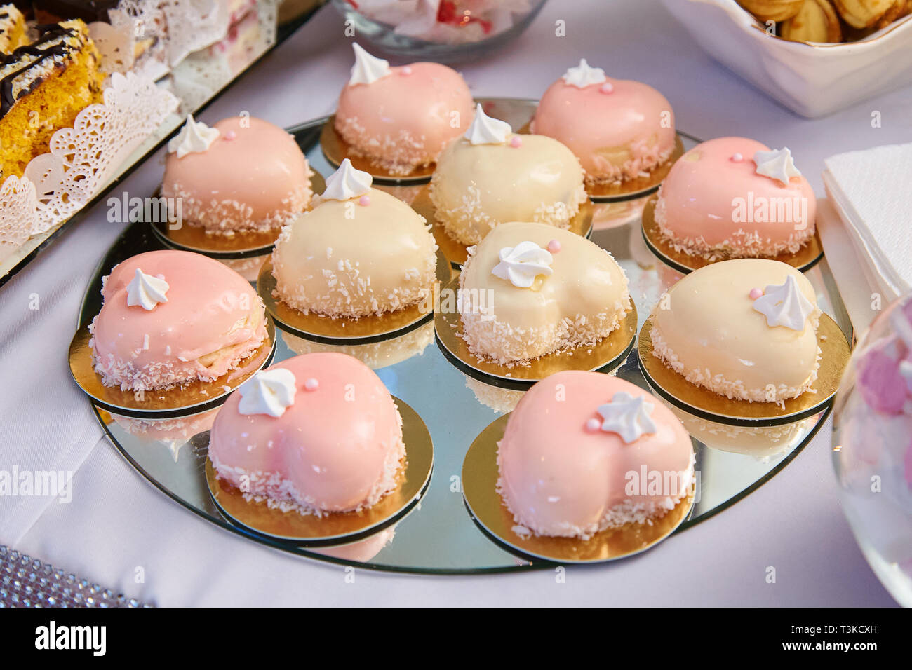 Moderne französische Mousse Kuchen mit rosa Spiegelglasur in Form eines Herzens auf einem Tisch. Grußkarte zum Valentinstag oder Geburtstag. Kuchen in Form eines W Stockfoto