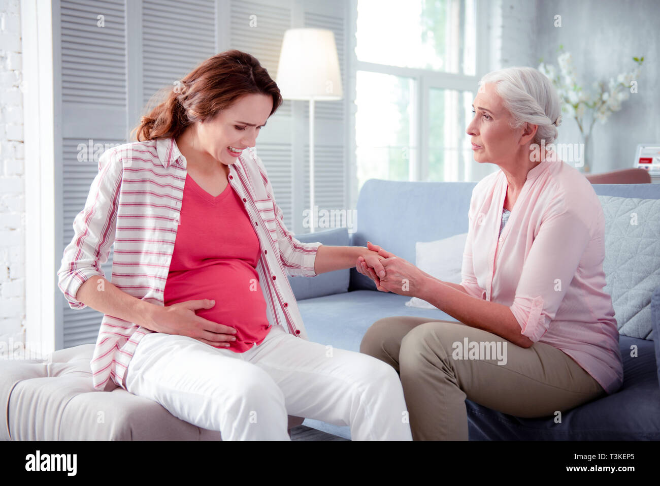 Grauhaarige Frau mit Hand ihrer schwangeren Tochter Stockfoto