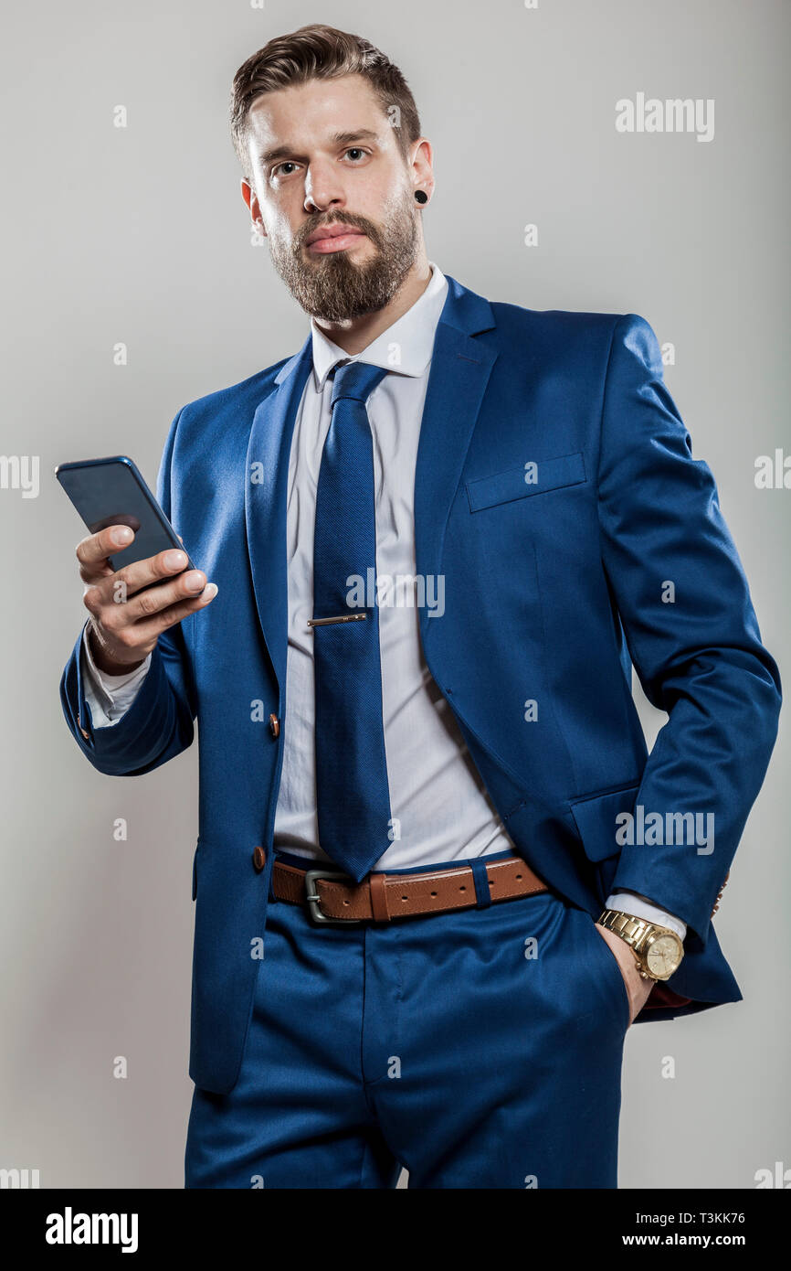 Porträt eines Geschäftsmannes in blauen Anzug Hemd Krawatte golden Luxusuhr  holding Smartphone Suchen in die Kamera gegen den grauen Hintergrund Glück  isoliert Stockfotografie - Alamy