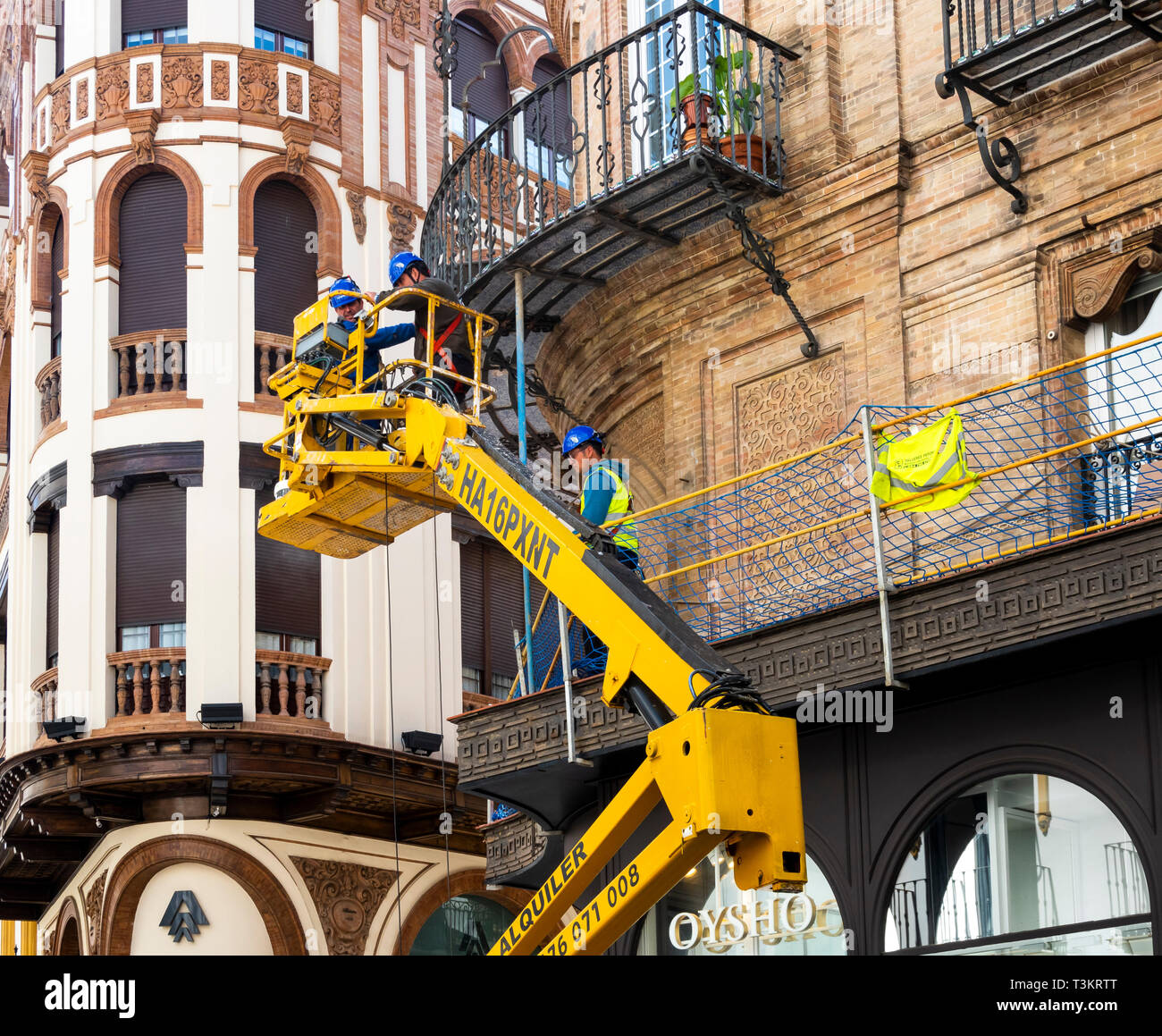 Drei Männer auf einer Houlotte HA 16 PX Einziehwerk Reparatur einer Metall Balkon in Sevilla, Spanien Stockfoto
