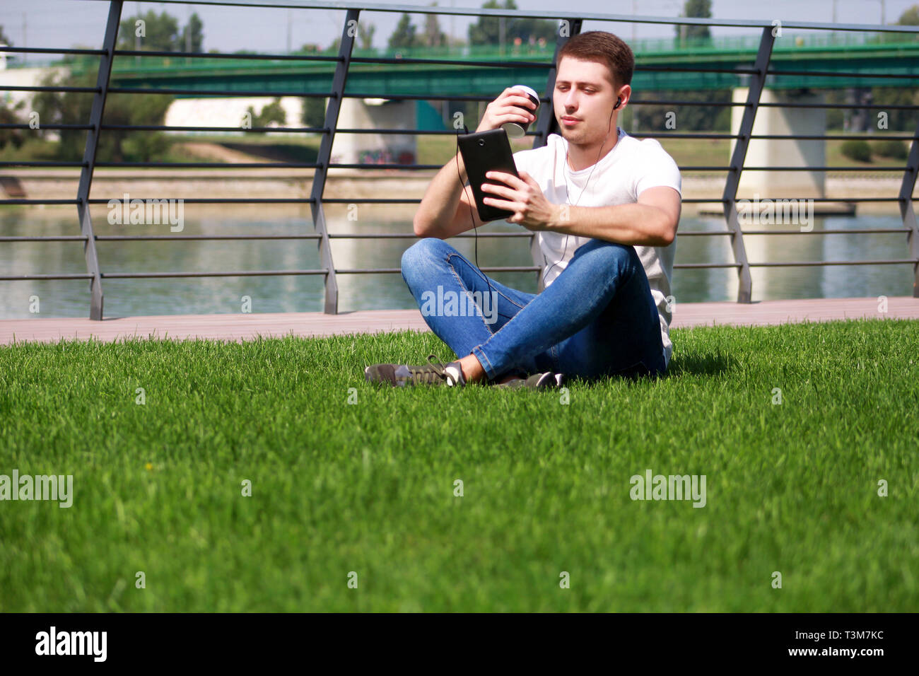 Schoner Junge Mit Tablet Und Kopfhorer Kaffee Trinken Zu Gehen Mann Sitzt Auf Gras Und Schone Sonnige Am Fluss Seite Modell Fotoshooting Stockfotografie Alamy