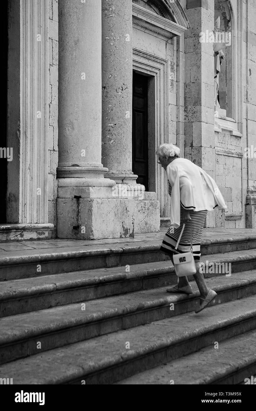 Frau steigt die Stufen zum Dom Eingang, Poljana Marina Držića, Dubrovnik, Kroatien. Schwarz und Weiss Stockfoto