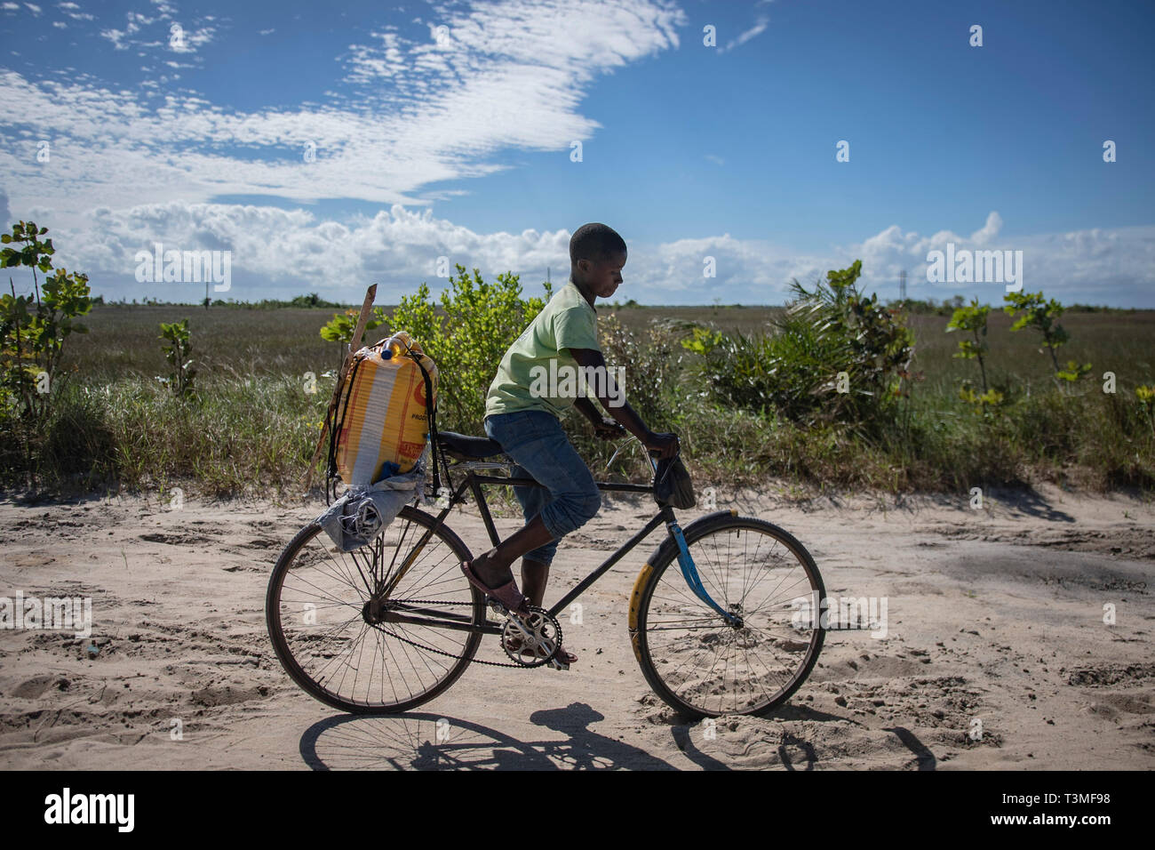 Ein Junge fährt mit dem Fahrrad in den Sand mit einem Sack von Nahrungsmittelhilfe für seine Familie in der Folge der massiven Cyclone Idai April 6, 2019 in Nhagau, Mosambik. Das World Food Programm, mit Hilfe von der US Air Force ist Transport der Hilfsgüter der verwüsteten Region zu unterstützen. Stockfoto