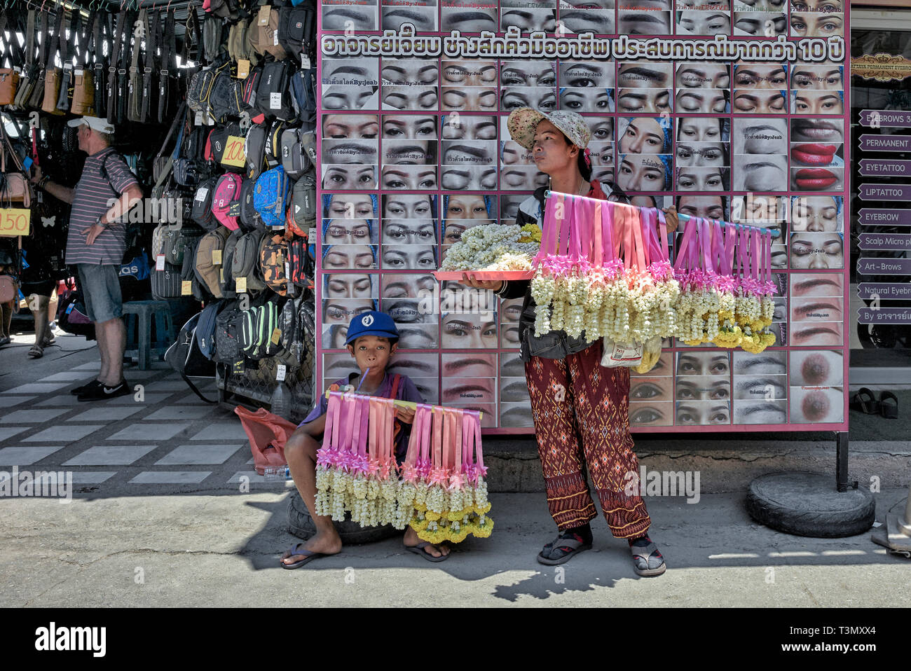 Thailand Straßenhändler. Mutter und Kind Verkauf von duftenden Blumen gegen eine auffällige Reklametafeln Stockfoto