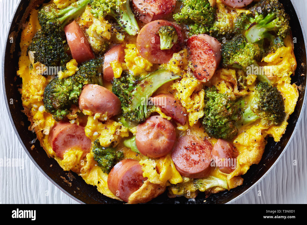 Leckere heiße Omelette mit Brokkoli und Würste in einer Pfanne bestreut mit frisch gemahlenem Pfeffer, horizontale Ansicht von oben, flach, Clos Stockfoto