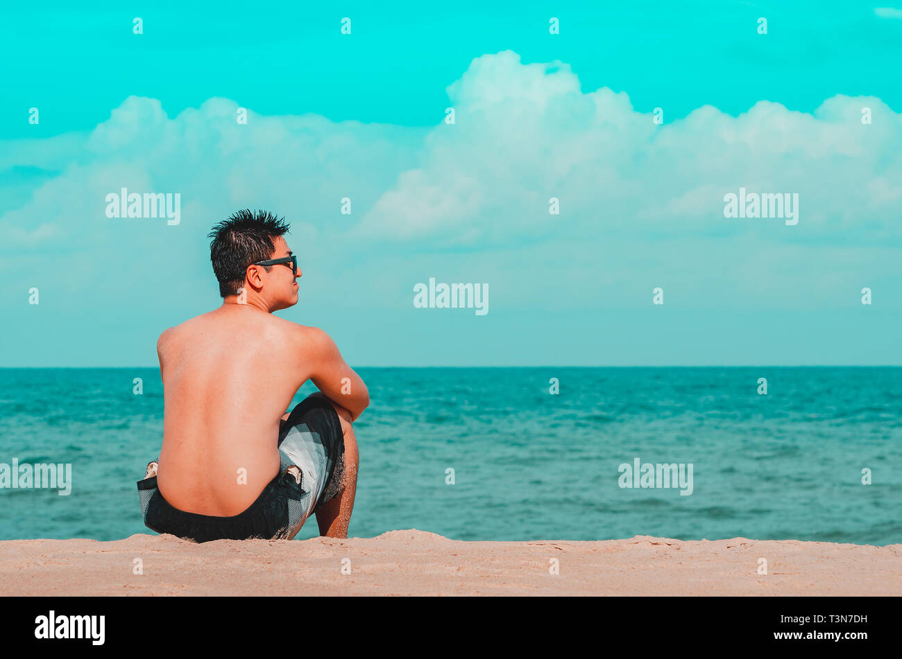 Mann auf der Sand am Strand sitzt, starrt auf das Meer. Cyan und orange Tönen. Foto bei Praia de Tabatinga 2, Conde PB Brasilien. Stockfoto