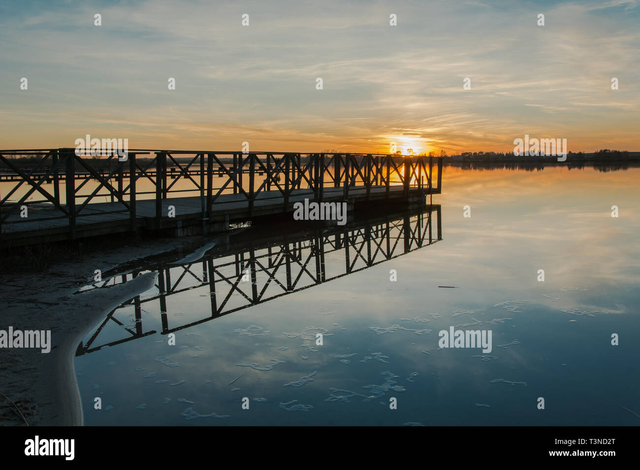 Hölzerne Brücke mit Geländer am Ufer des Sees und den Sonnenuntergang Sonne über dem Horizont Stockfoto