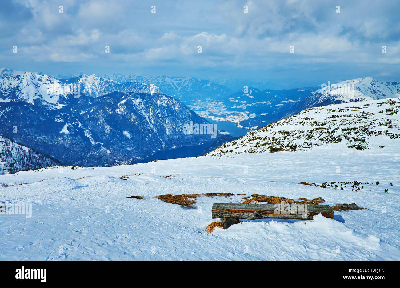 Die verschneite Holzbank am Hang des Dachstein-Krippenstein mit Blick auf Tal und neblig Hallstattersee Alpen im Inneren Salzkammergut, Österreich. Stockfoto