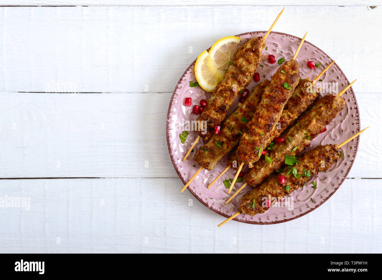 Lecker lula Kebab auf der Platte auf einem weißen Holztisch. Gehacktes Fleisch auf Holzspieße, gegrillt. Östliche Küche. Ansicht von oben, flach. Stockfoto
