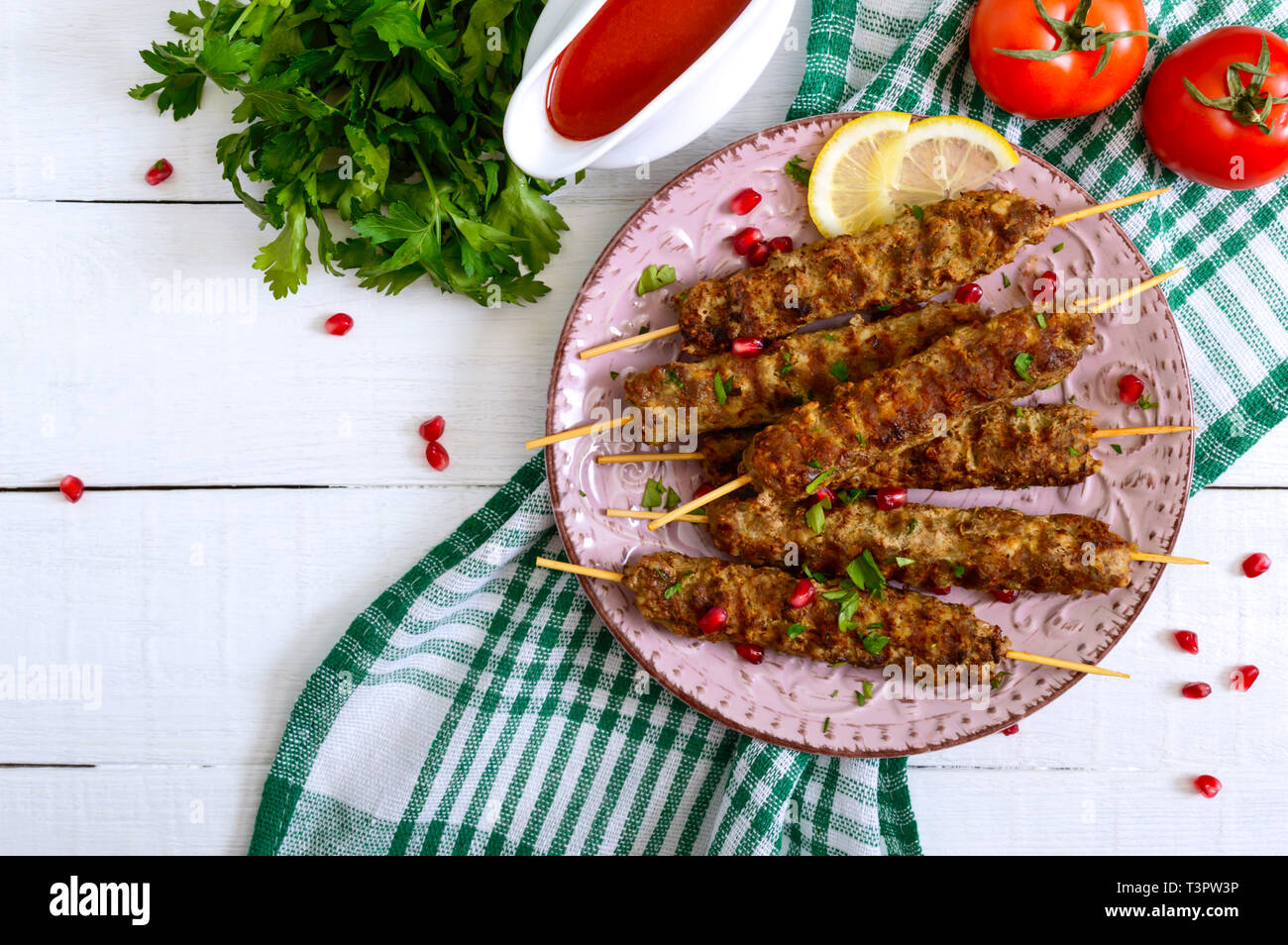 Lecker lula Kebab auf der Platte auf einem weißen Holztisch. Gehacktes Fleisch auf Holzspieße, gegrillt. Östliche Küche. Ansicht von oben, flach. Stockfoto