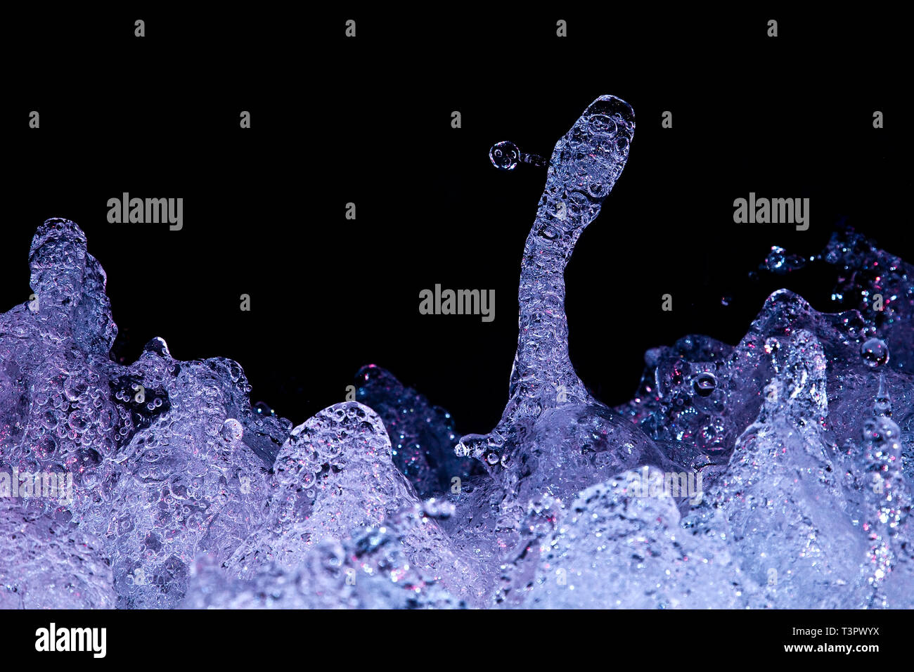 Blau beleuchtetes turbulentes Wasser bildet futuristische Formen, die von eingeschlossenen Luftblasen glitzern und sich wie eine außerirdische flüssige Skulptur vor einem schwarzen Hintergrund erheben. Stockfoto