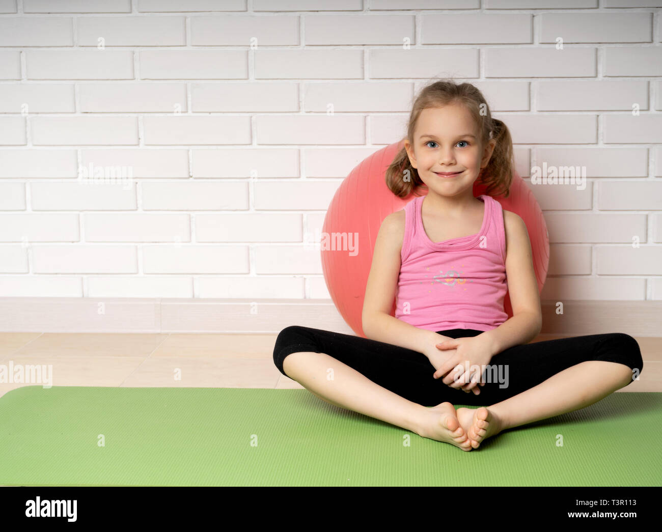 Fröhliches kleines Mädchen Ausruhen nach Sport Übungen Training auf der Matte zu Hause, Sport für Kinder und Yoga. Stockfoto