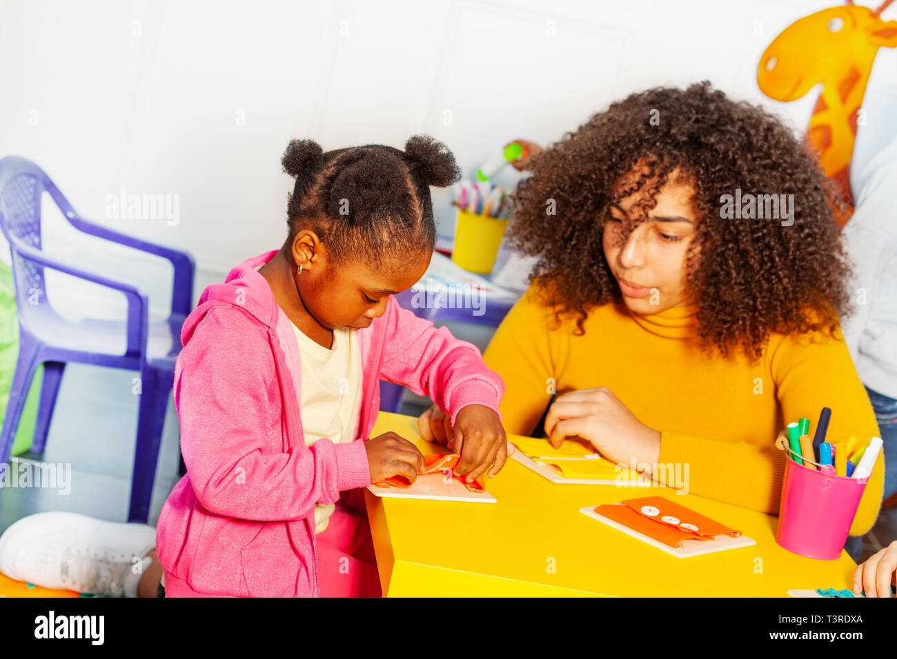 Mädchen im Kindergarten lernen zu Taste aufzuknöpfen Stockfoto