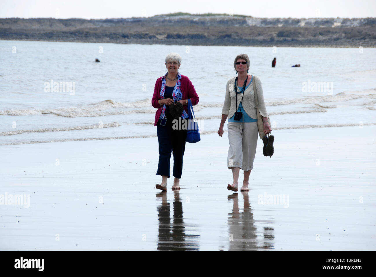 Zwei ältere Damen barfuß am Strand am Rande des Wassers Stockfoto