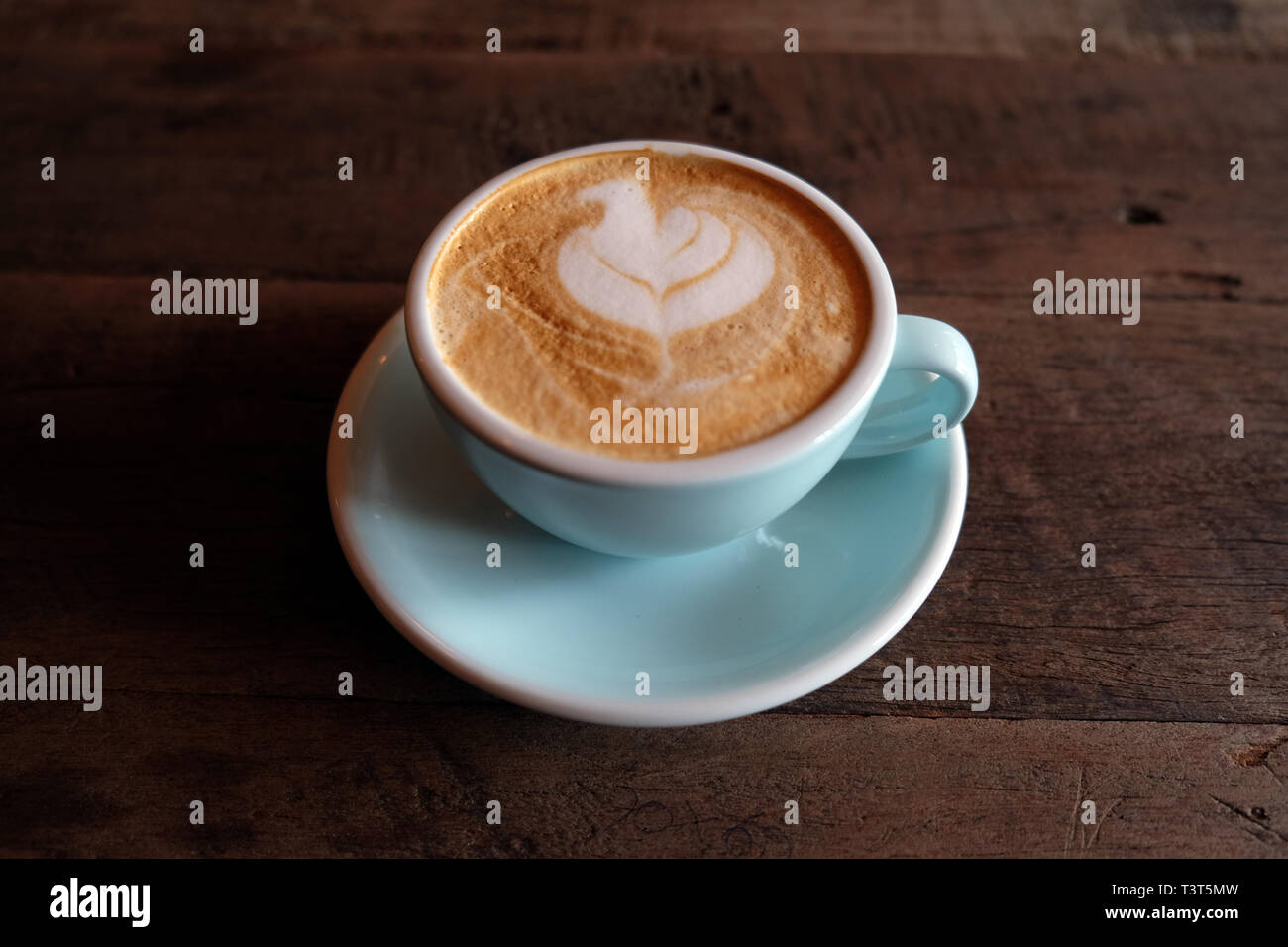 Cappuccino oder Latte mit aufgeschäumter Schaumstoff, blau Kaffeetasse oben auf hölzernen Coffee shop Hintergrund Stockfoto