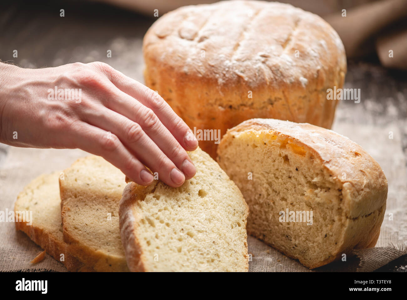 Frauen Hände brechen hausgemachten Naturprodukten frisches Brot mit einer goldenen Kruste auf eine Serviette auf einem alten Holz- Hintergrund. Das Konzept der Backen Backwaren Stockfoto