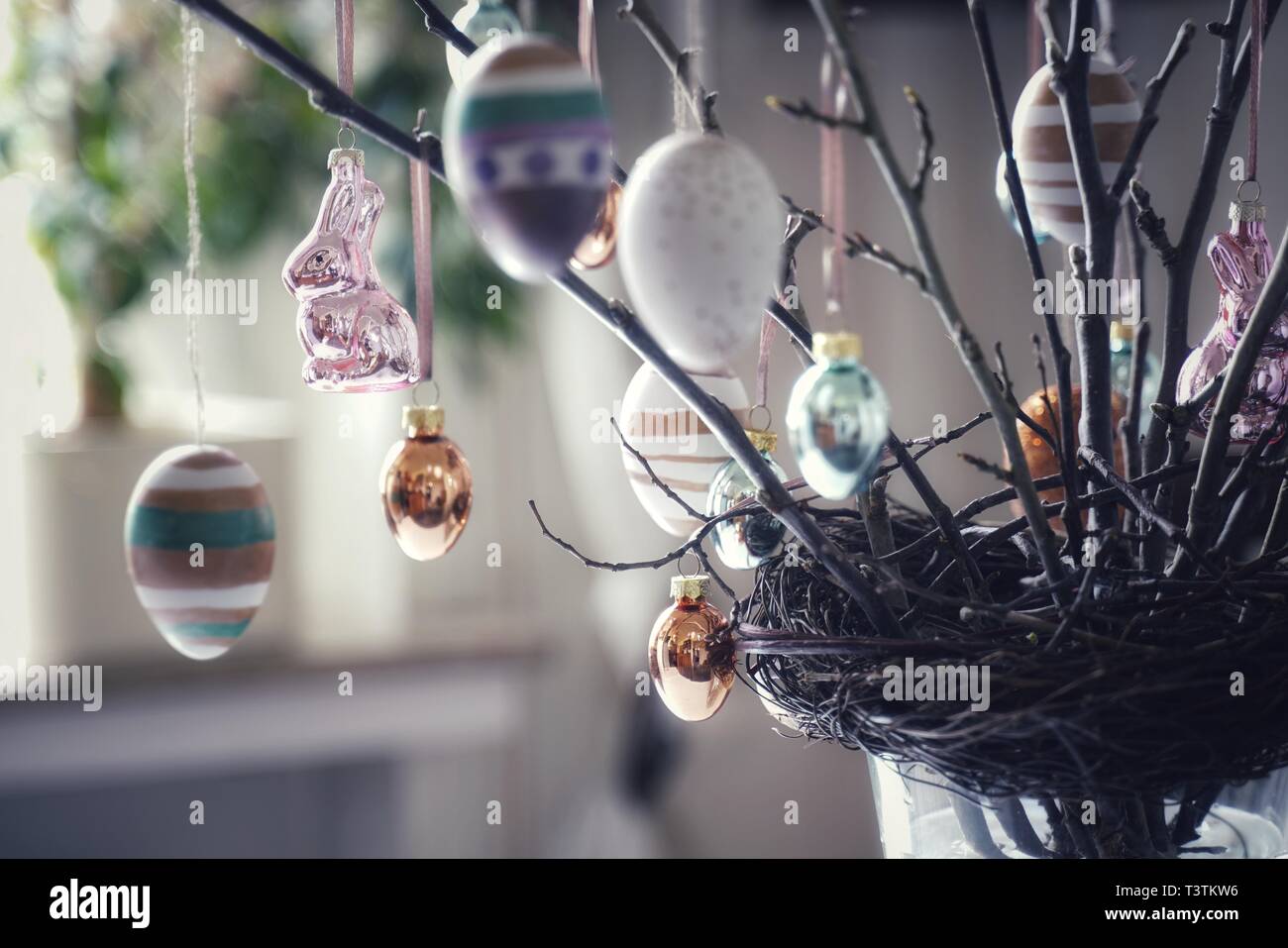 Zweige mit Knospen in einem Nest fest. Sie sind mit österlichen Motiven verziert. Handbemalte Ostereier und glänzend Osterhasen. Tischdekoration in Fron Stockfoto