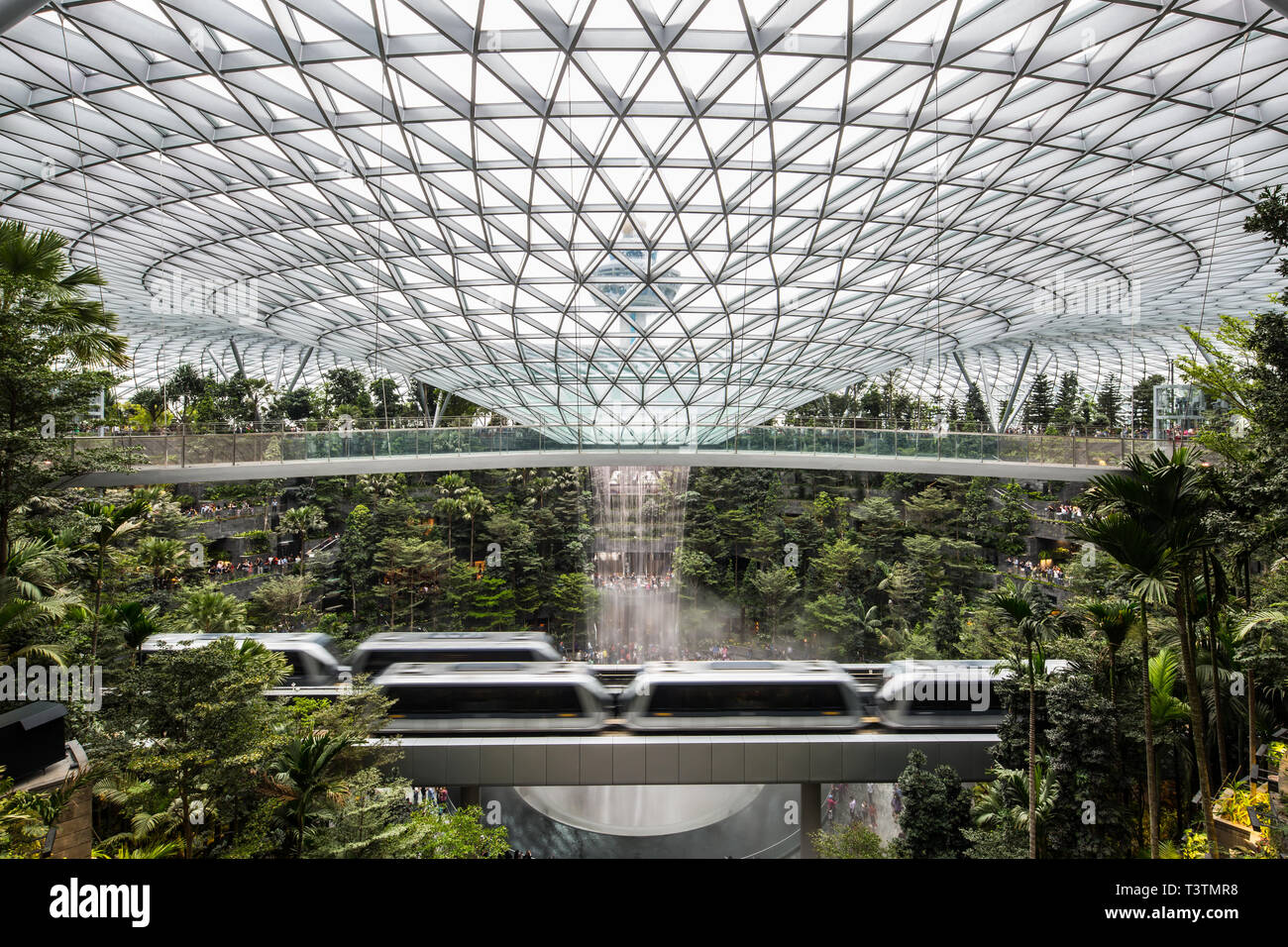 Eine weite Sicht auf die konvexe Struktur, die Wasser in das Untergeschoss des Jewel Changi Airport und den Flugsicherungsturm dahinter, Singapur, regnet Stockfoto