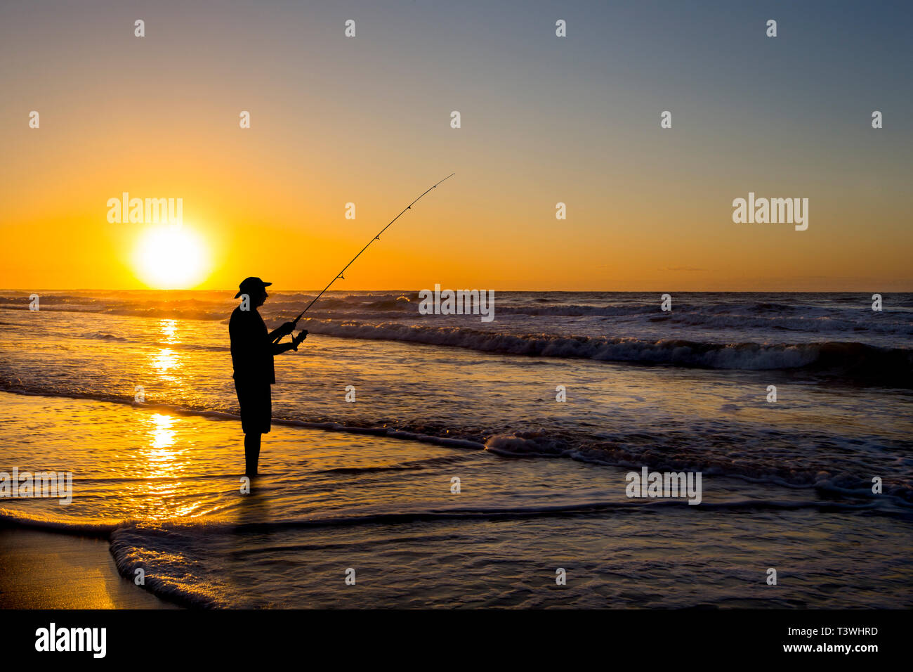 Silhouette der Mann Angeln in Wellen am Strand bei Sonnenuntergang Stockfoto