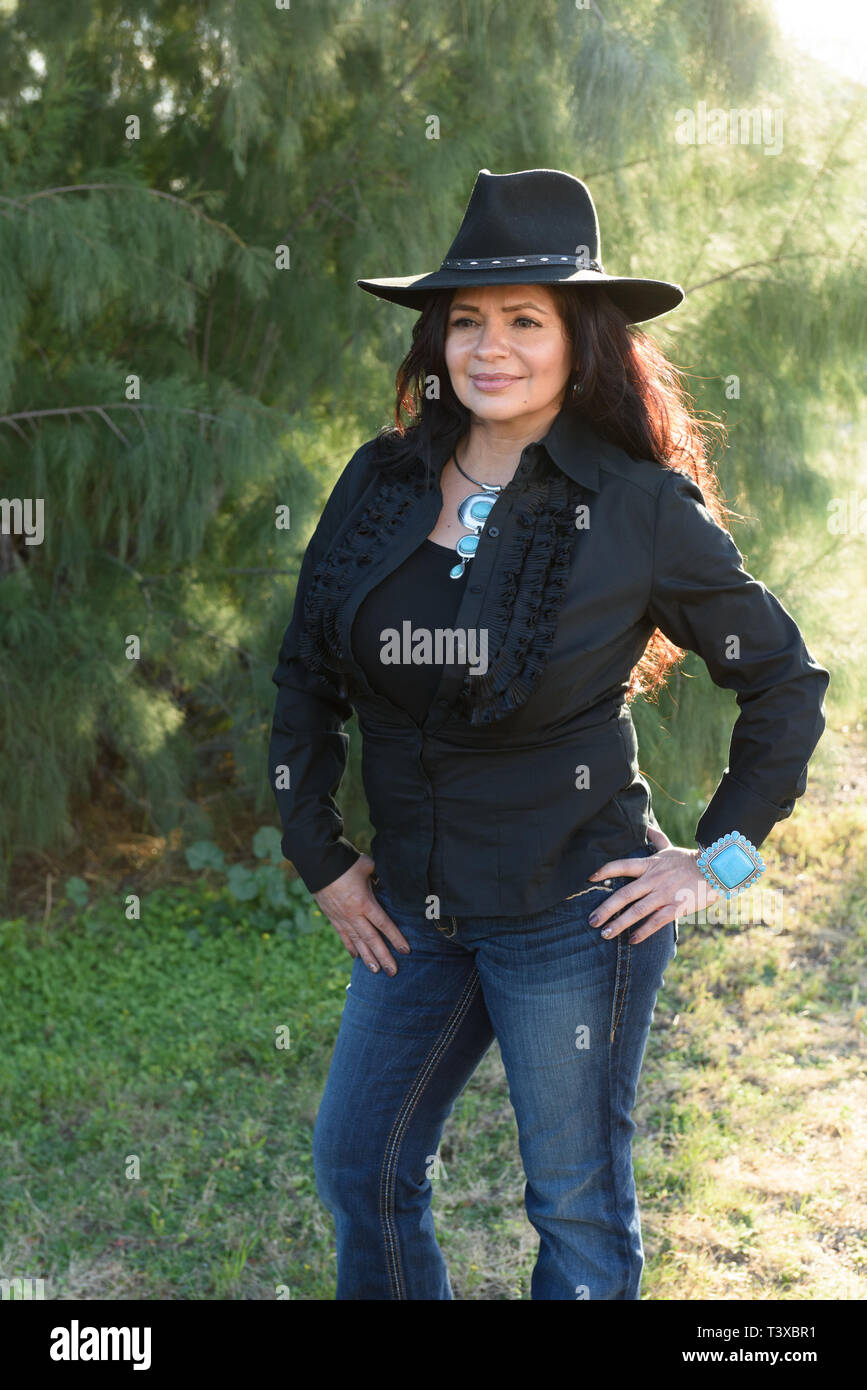 Cowgirl mit langen dunklen Locken in schwarzen Hut mit Sonnenlicht auf ihrem Rücken. Stockfoto