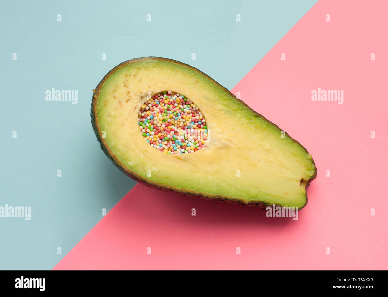 Halbierte Avocado gefüllt mit bunten Zuckerperlen auf blauem und rosafarbenem Hintergrund Stockfoto