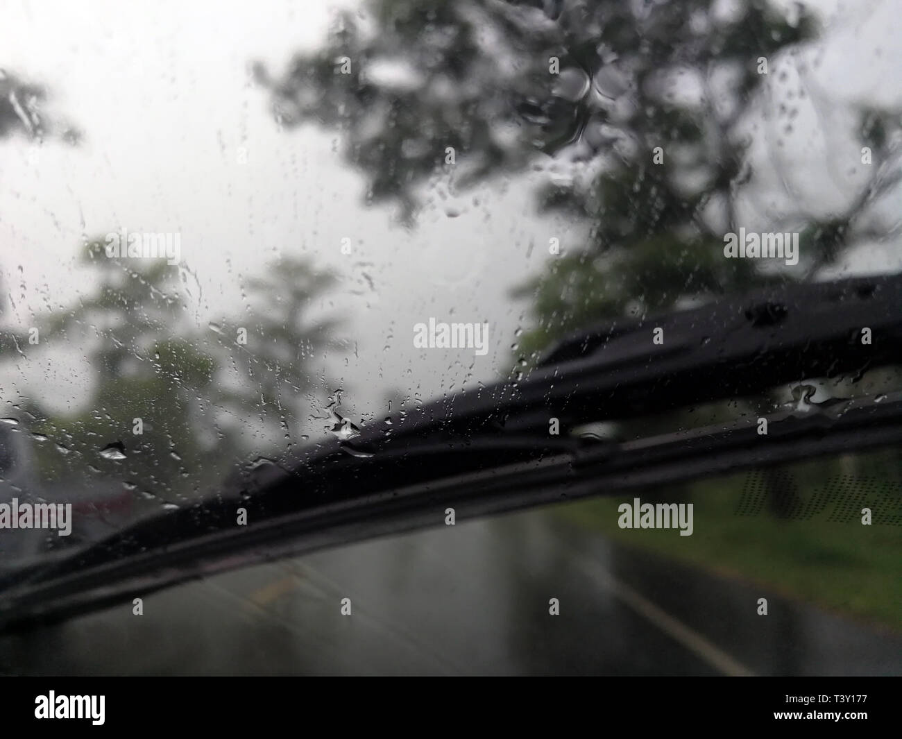 Regen fällt auf das Auto Glas Fenster mit Straße in der Regenzeit Abstract Background, Wassertropfen auf dem Glas, Nacht Sturm Regen Autofahren Konzept. Stockfoto