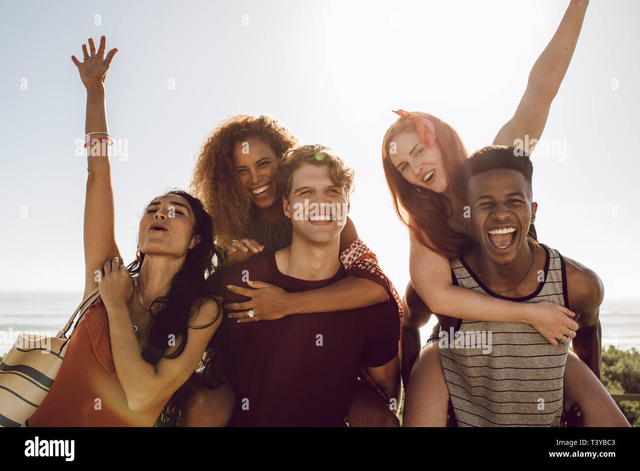 Männer huckepack Frauen im Freien und Spaß haben. Gruppe von multi-ethnischen Menschen Spaß an einem Sommertag. Stockfoto