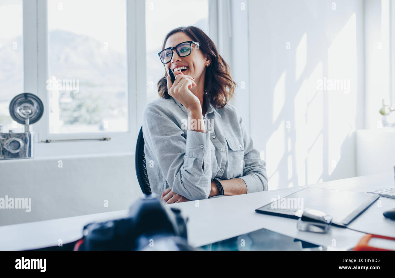 Weibliche Creative Professional an ihrem Schreibtisch sitzen und Lächeln. Fotografin in ihrem Büro. Stockfoto